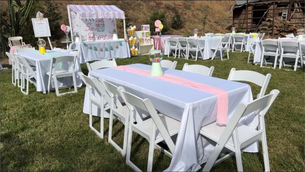 Outdoor party with white tables, chairs, and a pastel candy-themed dessert station